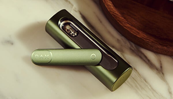 Geöffneter Pax Flow Vaporizer Nahaufnahme des geöffneten Pax Flow Vaporizers, das die mit Cannabis gefüllte innere Kammer zeigt, gehalten von einer Hand in einer entspannten Outdoor-Umgebung mit natürlichem Licht.