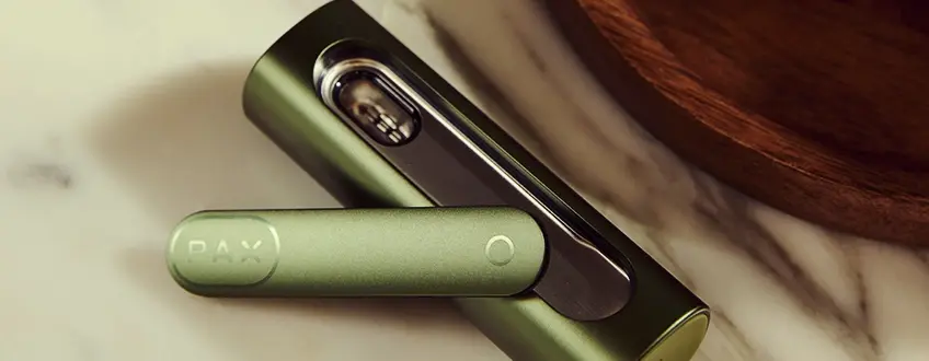 Geöffneter Pax Flow Vaporizer Nahaufnahme des geöffneten Pax Flow Vaporizers, das die mit Cannabis gefüllte innere Kammer zeigt, gehalten von einer Hand in einer entspannten Outdoor-Umgebung mit natürlichem Licht.
