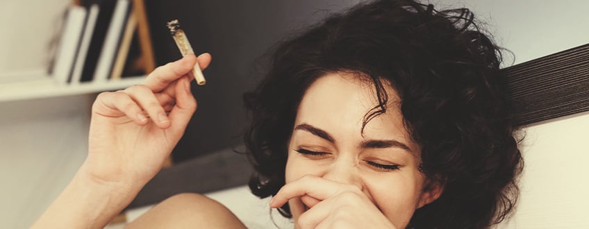 Person, die lachend einen Cannabis-Joint hält.