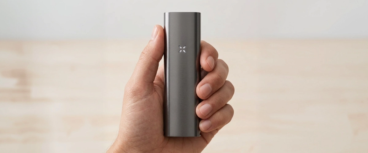 Produktansicht des PAX Four Vaporizers in der Hand PAX Four Vaporizer in einer Hand gehalten, mit schlankem mattem Gehäuse, kompakter Größe und LED-Blütenblattanzeige auf der Vorderseite
