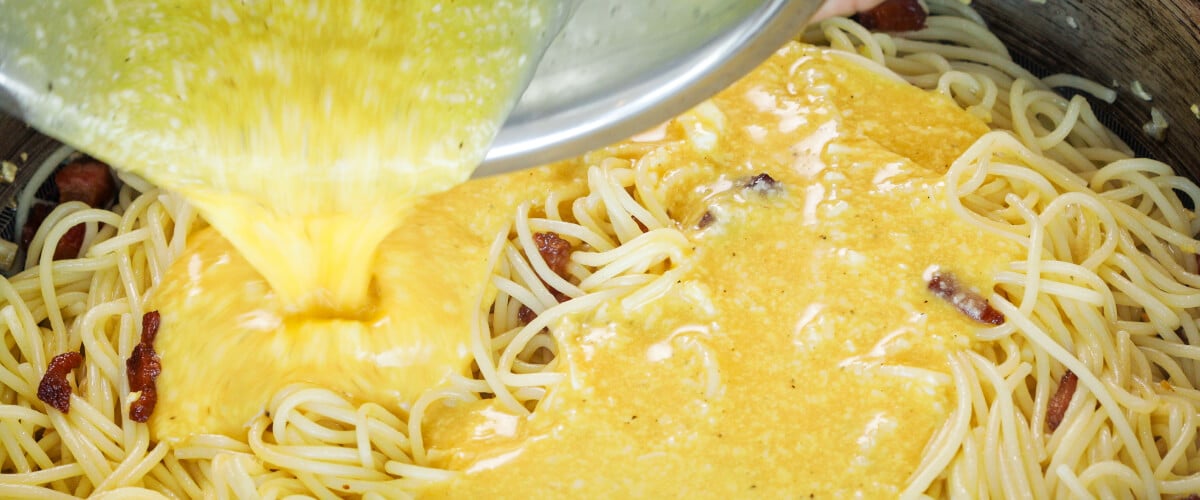 Eier-Käse-Mischung wird über heiße Spaghetti in der Pfanne gegossen, fünfter Schritt für eine Cannabis-Carbonara