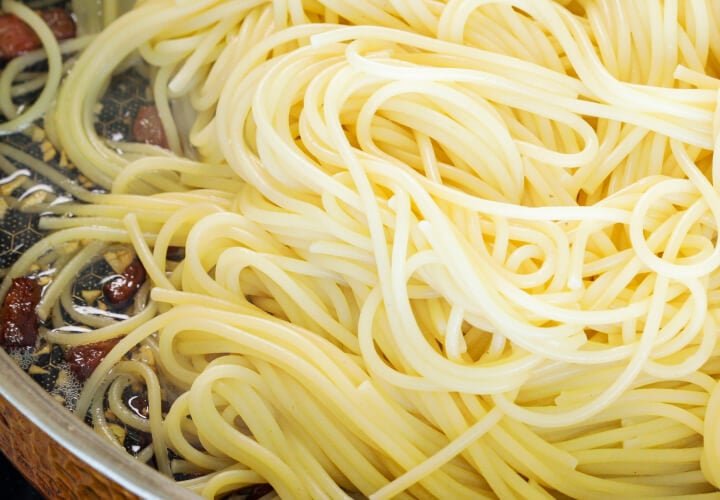 Abgetropfte Spaghetti werden mit knuspriger Pancetta und infundierter Butter in der Pfanne vermengt, vierter Schritt für eine Cannabis-Carbonara